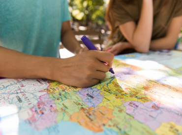 Imagem ilustrativa mostra braços de jovens estudantes realizando anotação em mapa da Europa